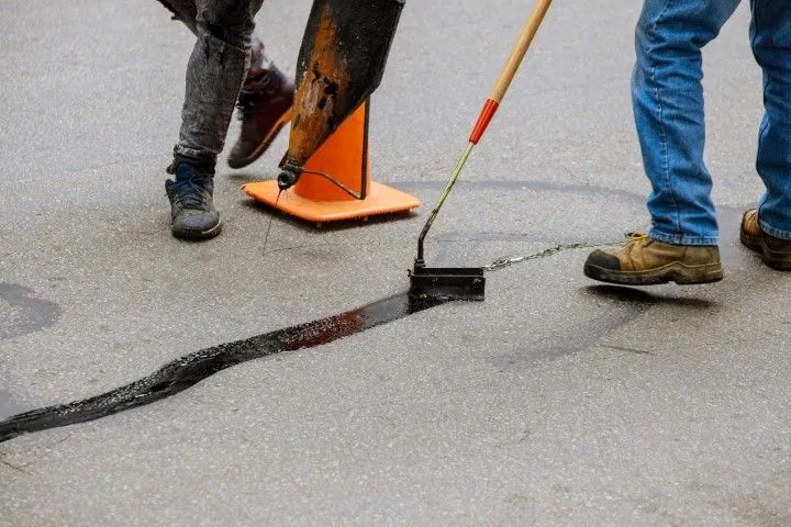 Concrete repair workers filling crack in pavement with safety cones in Grandview, MO